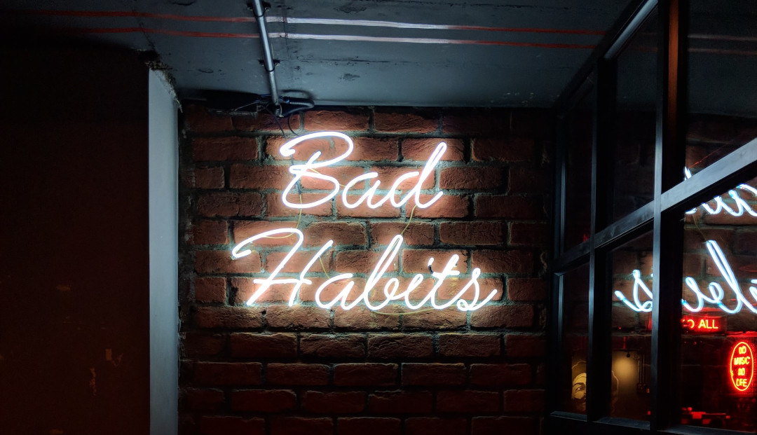 Photo of a neon sign with the words, 'Bad Habits' in a lounge type setting