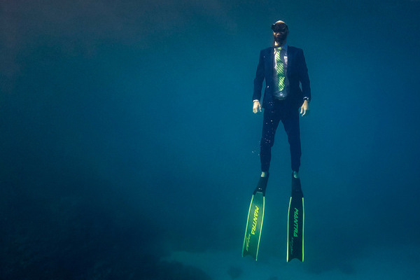 Costa Michailidis diving underwater in a full business suit, cufflinks and all